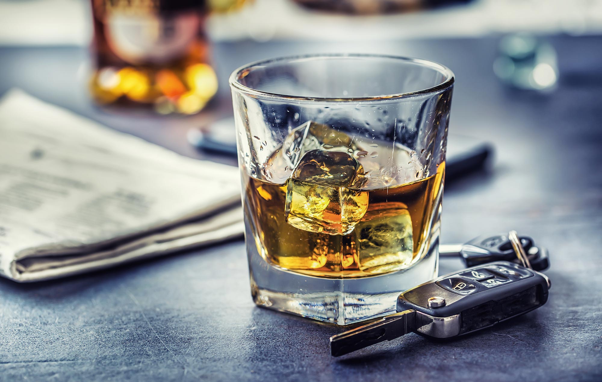 A small glass of ice and whiskey sits next to a set of car keys.