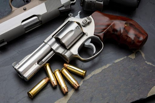 A revolver sits on a gray-colored table. Brass bullets are scattered next to it.