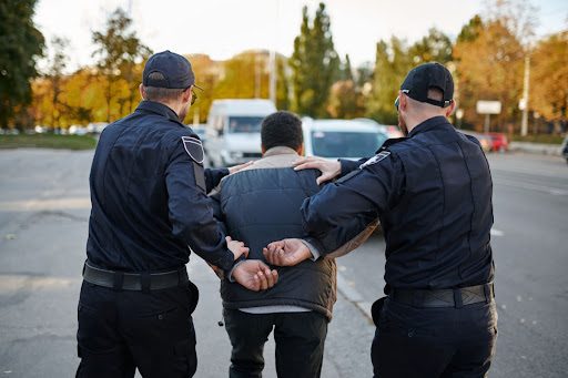 A man is arrested and being taken to a police car by two officers. He has committed a crime and is now facing punishment.