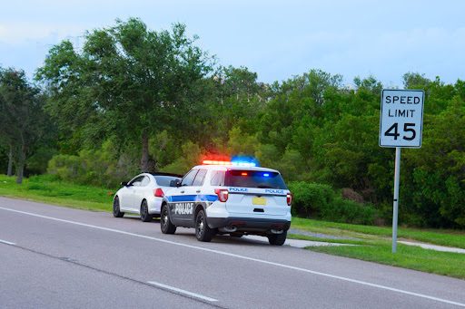 A police car has a driver pulled over after a speed limit sign.