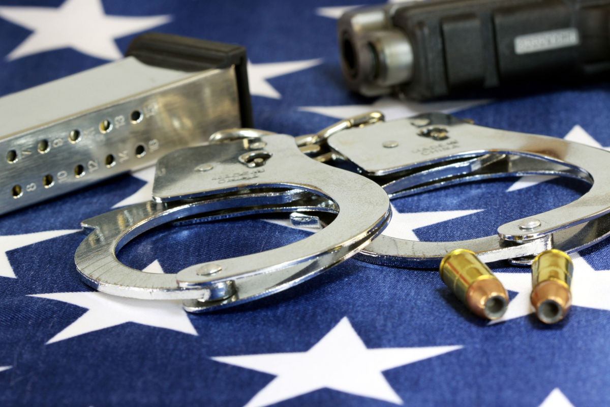 A gun sits next to handcuffs, bullets, and the American Flag.